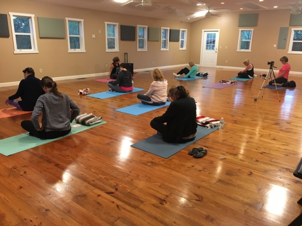 yoga room full of women sitting on the floor praying in a yoga class