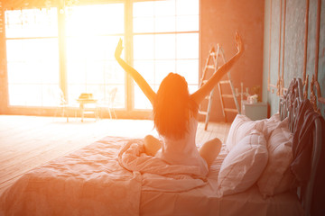 girl sitting on a bed waking up with the sun shining into her window