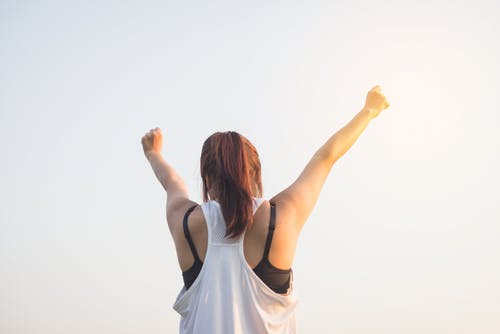 Girl standing outside with a workout outfit and reaching to the sky