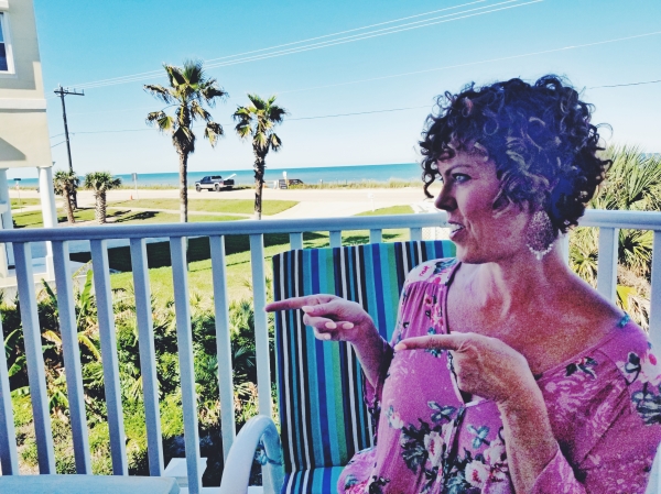 GG on her patio overlooking and pointing to the ocean